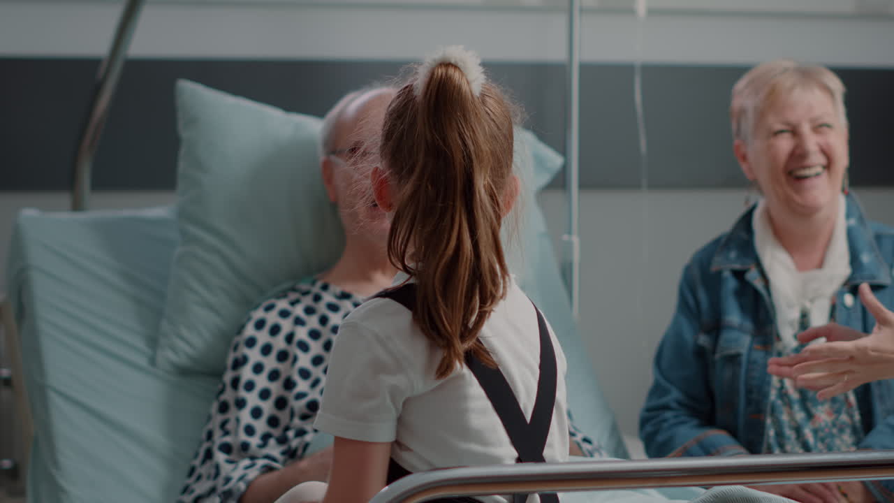 Close up of little girl visiting pensioner with illness in hospital ward bed