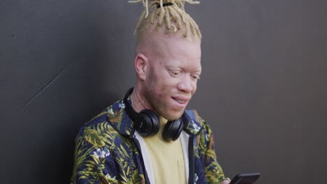 Portrait-of-smiling-albino-african-american-man-with-dreadlocks-using-smartphone