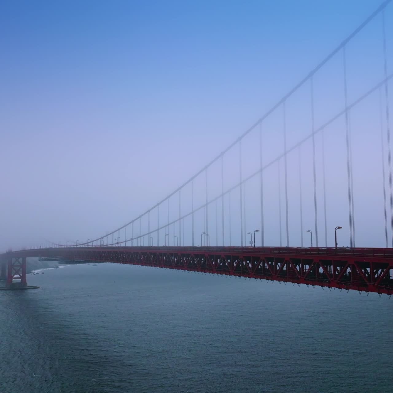 Cars moving quickly by the long Golden Gate Bridge. Amazing structure of San Francisco in the thick fog