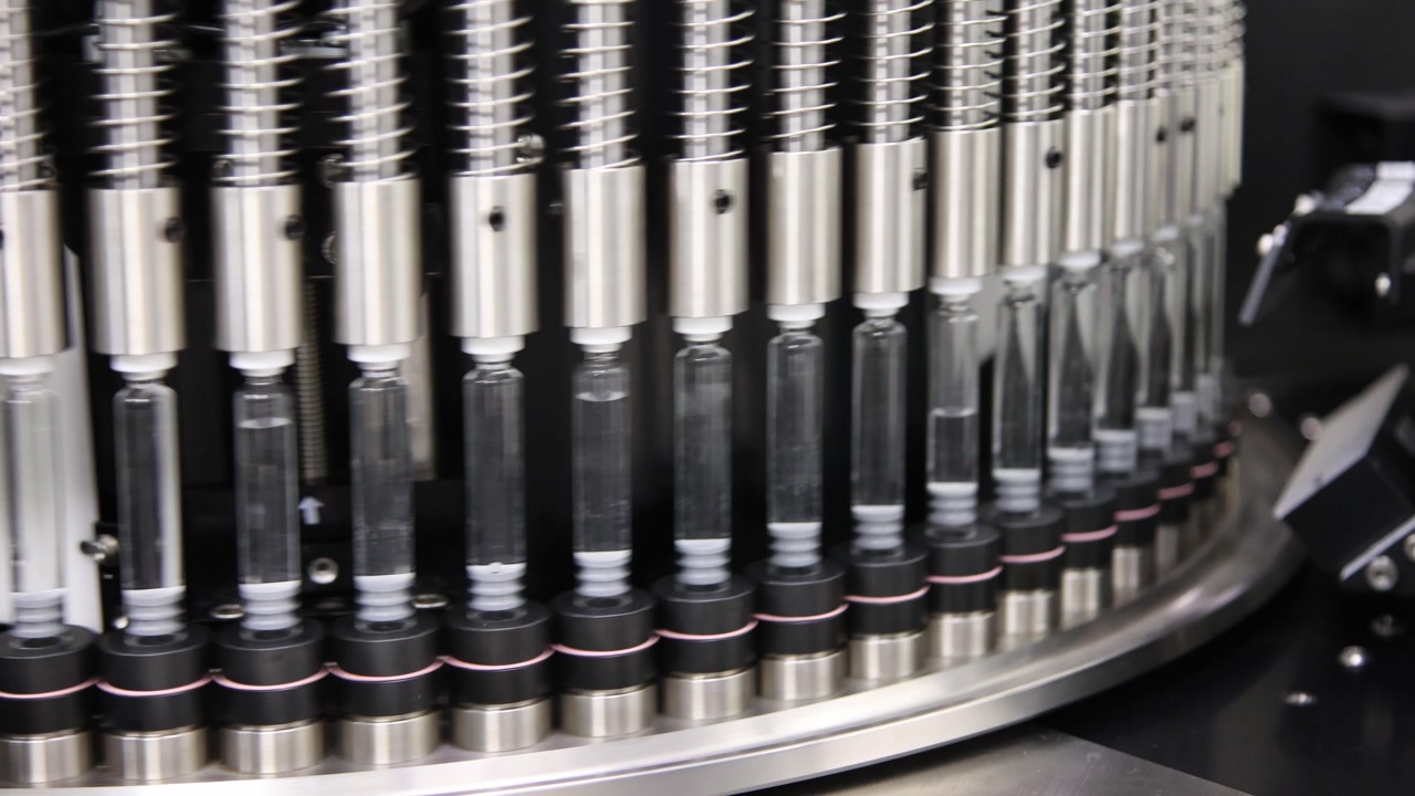 A detailed view of an industrial rotary machine filling and sealing glass ampoules with liquid medication in a sterile pharmaceutical manufacturing plant.