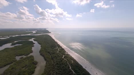 delnor-wiggins beach. high aerial footage shows all the tree surrounding, sandy yellow beach and sun reflecting off the sea. naples, florida.