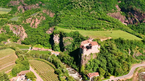 bright sun illuminates runkelstein castle on the unapproachable rock. green scenery of vineyards in bolzano, south tyrol, italy. aerial view.