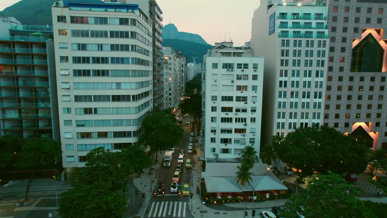 Panorâmica aérea de drone para a esquerda sobre o bairro de Copacabana, ao anoitecer, Rio de Janeiro, Brasil. Resorts e hotéis à beira-mar na avenida principal.