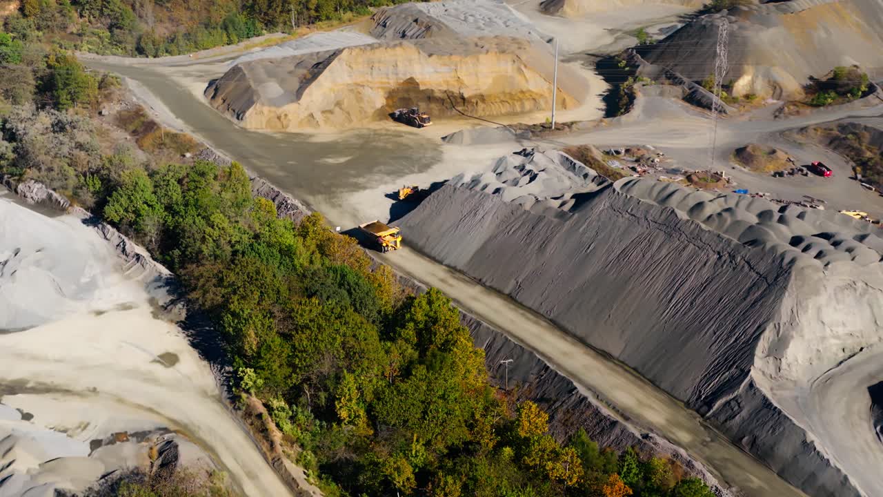 Aerial angled pullback of dump truck driving below gravel stockpiles on haul road at Jones Mill Quarry Arkansas USA