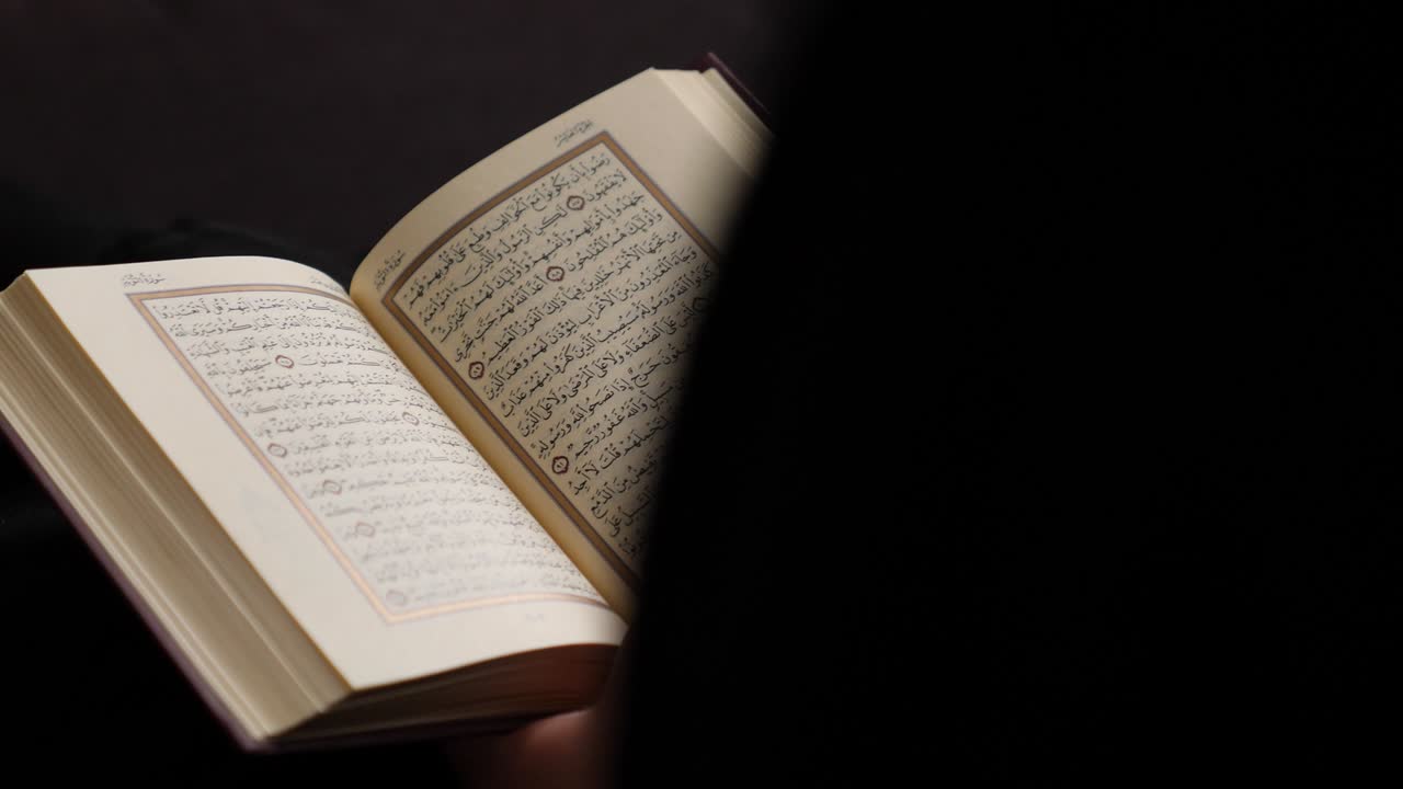 una persona musulmana leyendo el corán, el disparo se mueve a la izquierda detrás del lector y revela el corán en sus manos