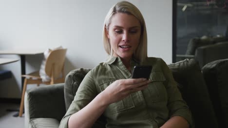 caucasian businesswoman sitting on couch using a smartphone in modern office