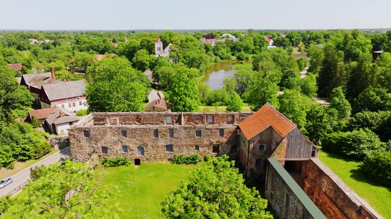 Aerial shows Aizpute Castle ruins and surrounding summer countryside Latvia