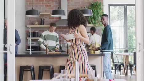 happy mixed race woman holding bowl while cooking with group of friends