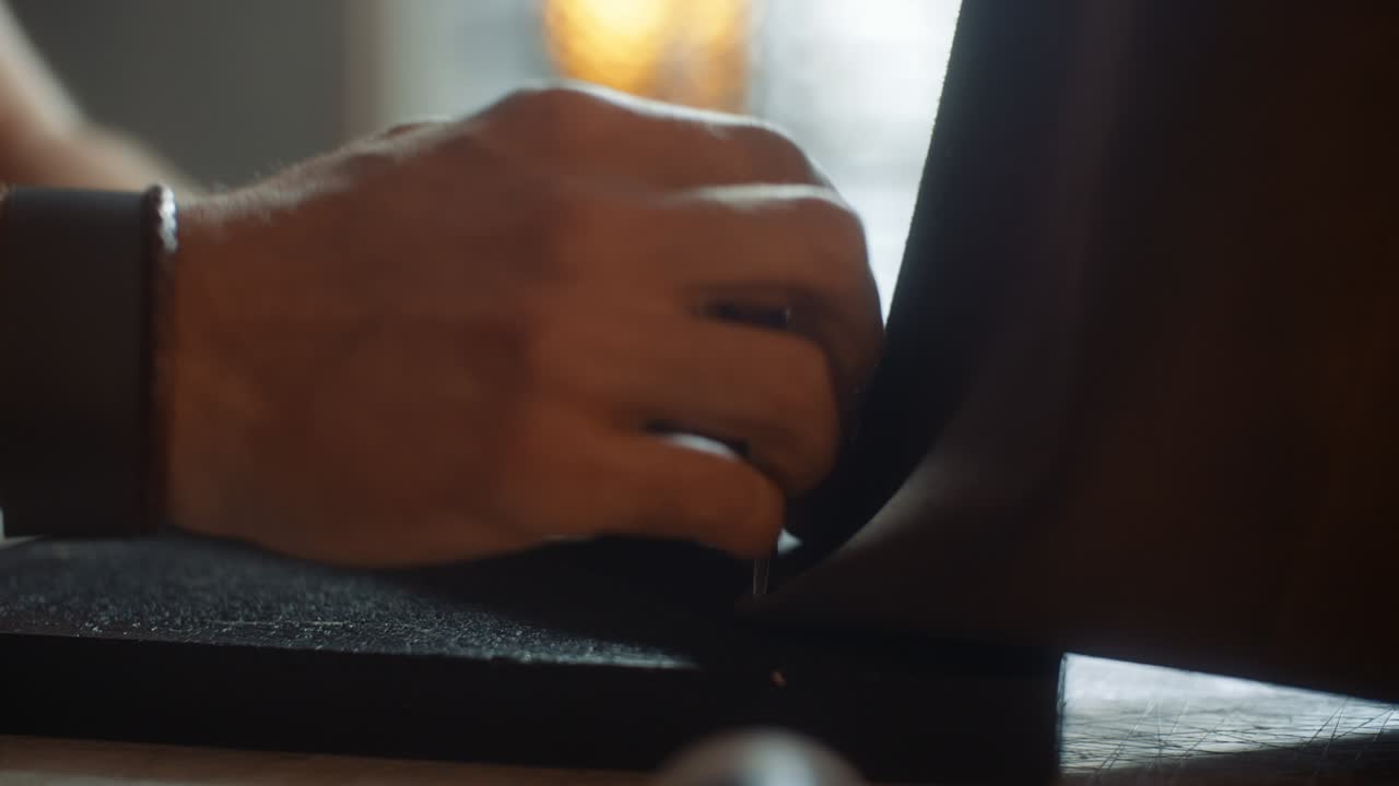 Side view of artisan hammering holes in leather handbag with leather punch