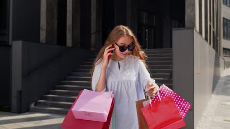 Girl-walking-from-mall-with-shopping-bags-and-talking-on-mobile-phone-about-sale-on-Black-Friday