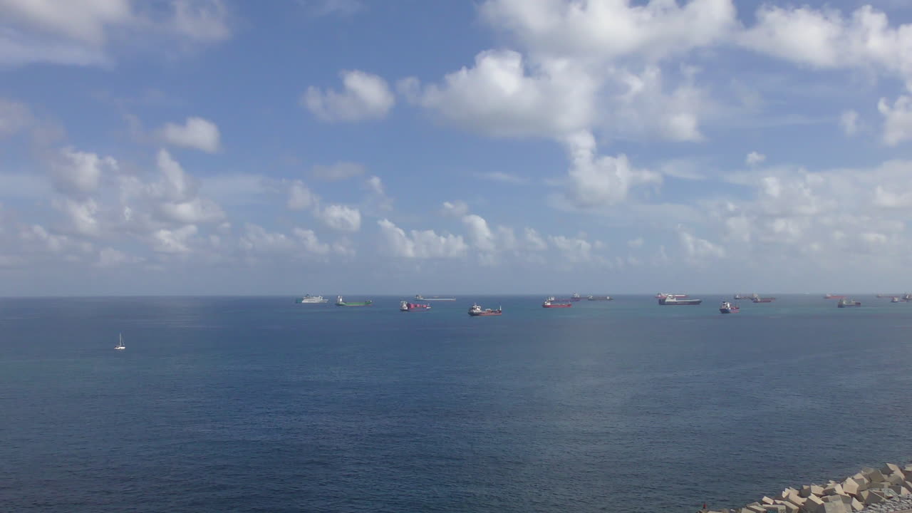 Many ships are anchored off a harbor in the roadstead