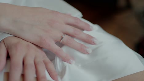 Close-up-of-a-woman's-hands-resting-on-a-white-satin-fabric,-with-a-diamond-ring-on-her-finger