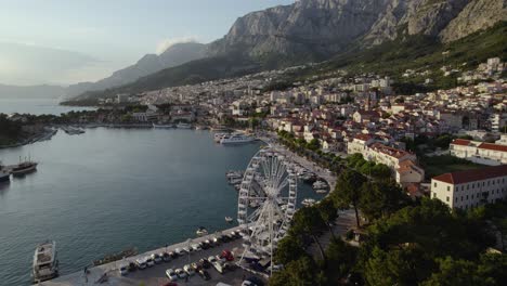 Makarska-with-ferris-wheel,-coastal-town,-and-mountains,-aerial-view