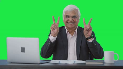 Happy-senior-Indian-businessman-showing-victory-sign-Green-screen