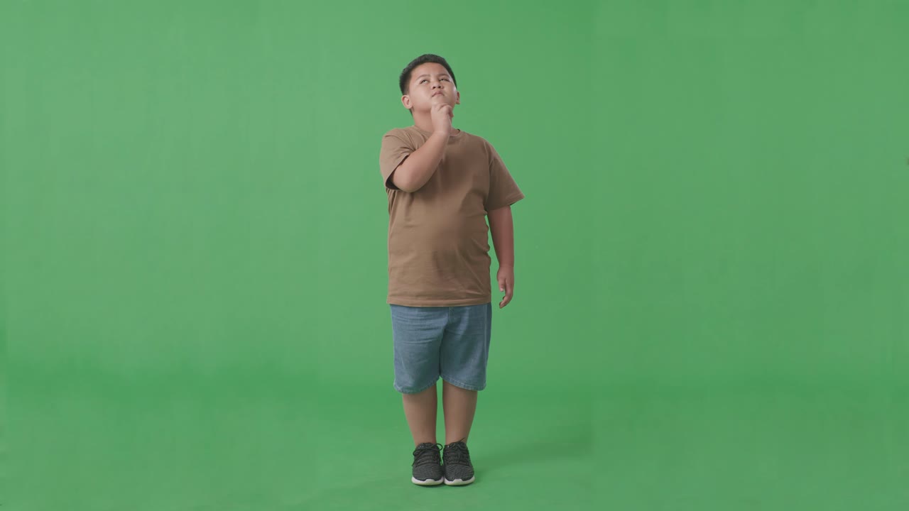 무언가를 생각하고 스튜디오의 녹색 화면을 둘러보는 아시아 소년의 몸이 가득 차 있습니다.