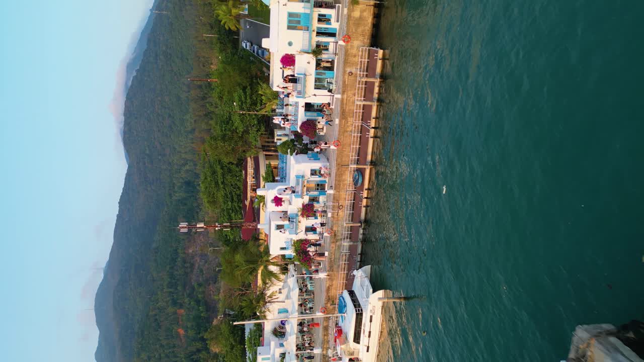 Tourists enjoying Son Tra greek themed mediterranean-style resort marina in Da Nang, Vietnam, vertical pulling out drone shot