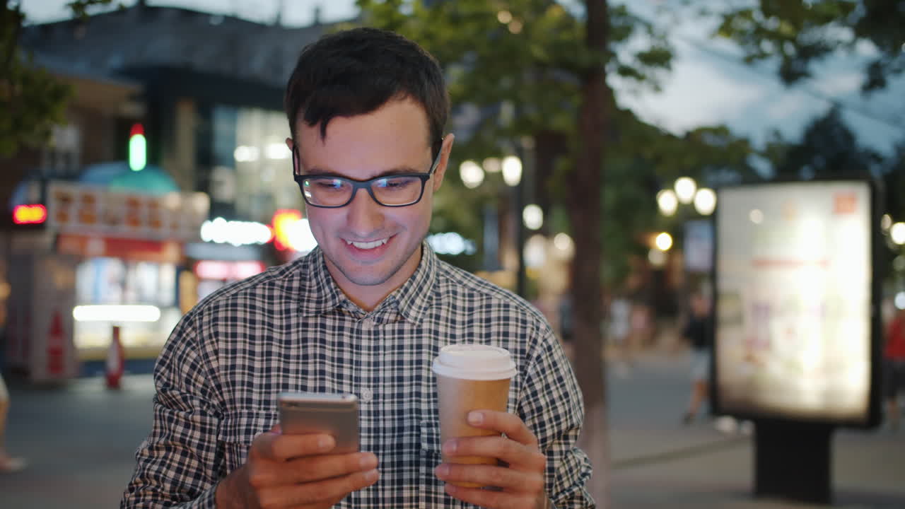 Man using smartphone and drinking coffee in city at night