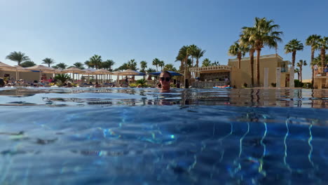 young woman in sunglasses in a sparkling blue swimming pool at a tropical location