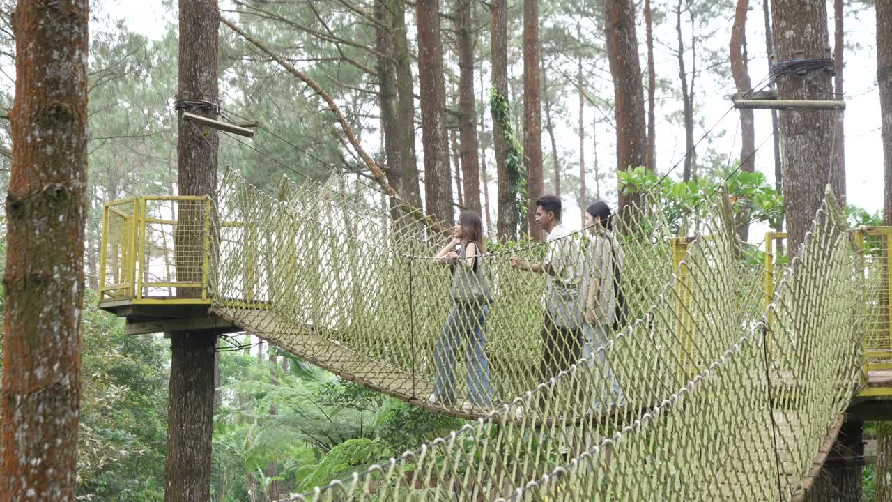 Young Asian Friends Crossing Rope Bridge in Forest Adventure