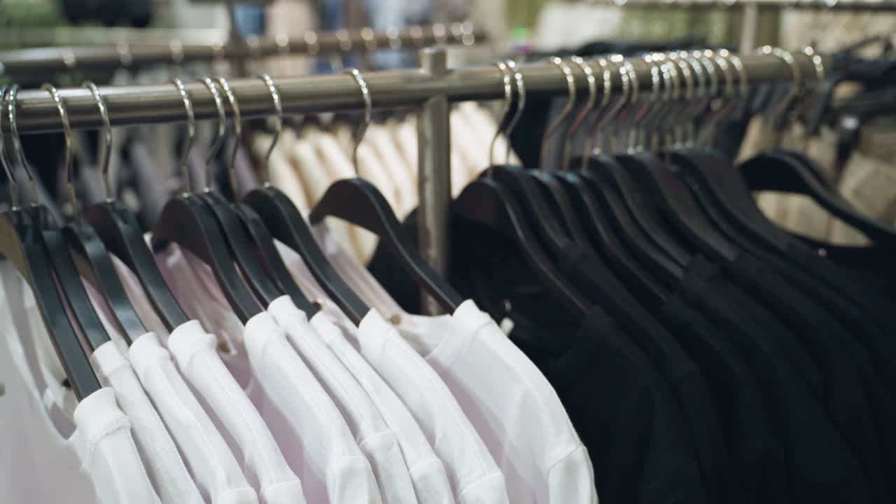 하색과 검은색의 셔츠를 끔하게 배열한 의류 가게 - 이 비디오는 현대 소매 환경에서 조직된 디스플레이와 다양한 의류를 강조합니다.