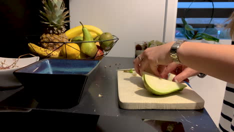 girl cutting a pear on a wooden board on the black tabletop