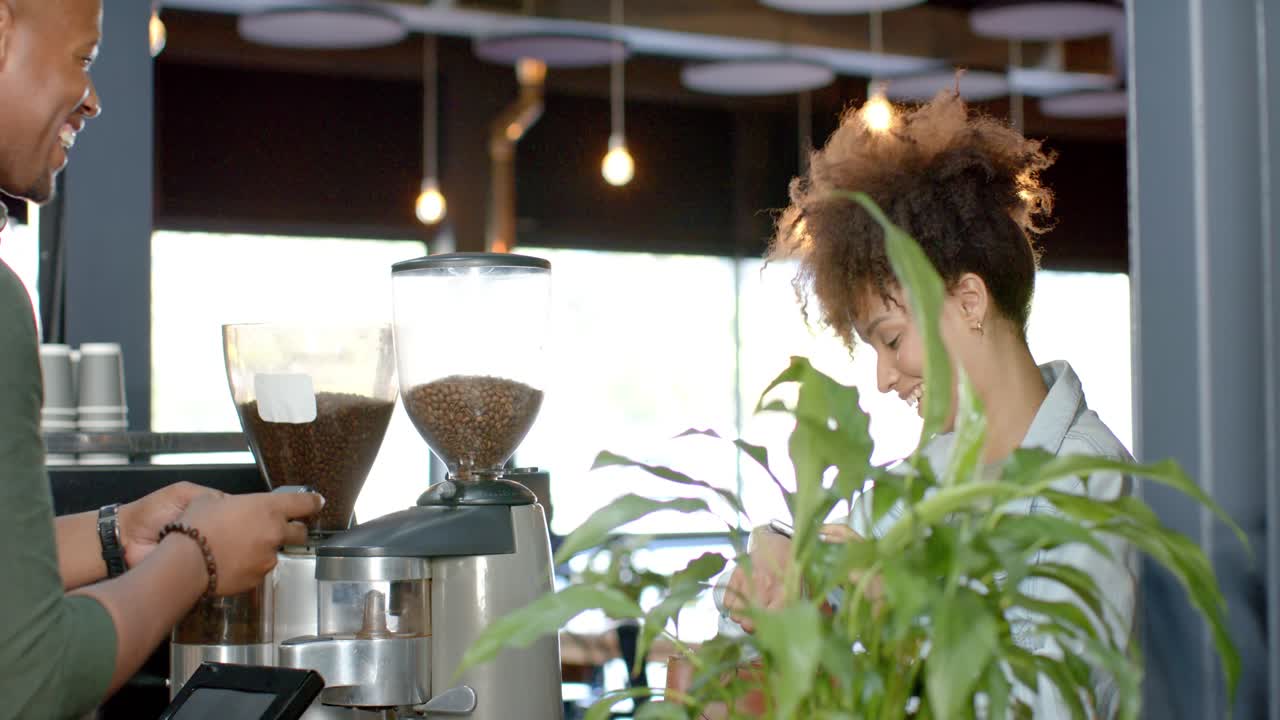 Un cliente guarda l'orologio al bancone del servizio, mentre il barista regola il macinacaffè e prepara un espresso.