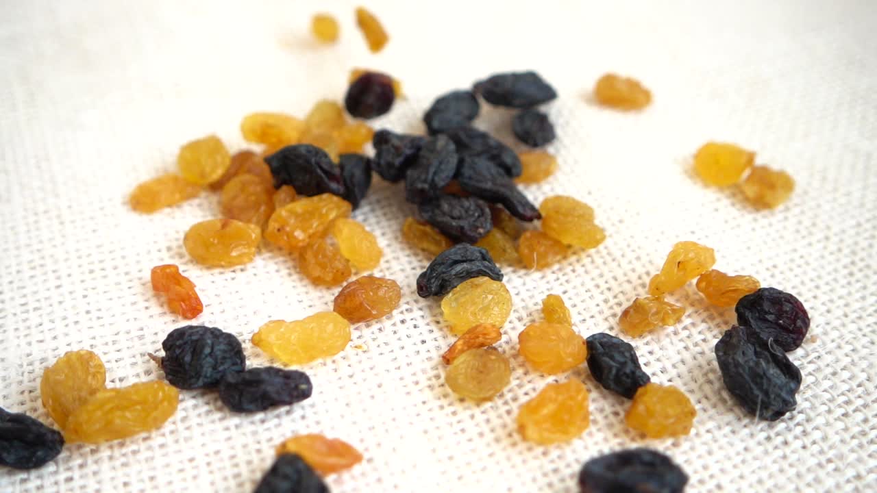 Raisins secs clairs et foncés. Filmés en tombant sur un sac. Ralenti