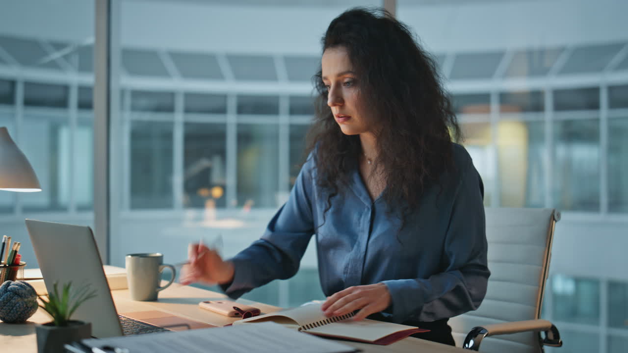 Focused woman working desk in evening closeup. Curly busy employee using laptop