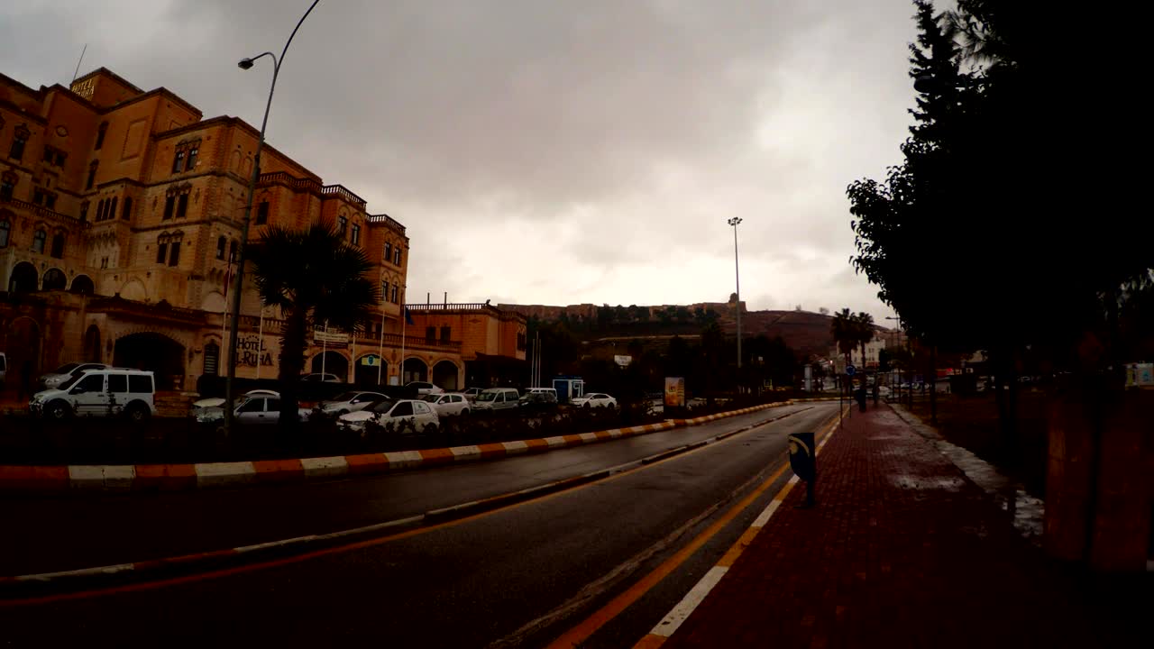 en el centro del edificio de shanlyurfa los coches conducen por la carretera de asfalto por la noche nublada