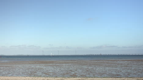 wide view of the dutch coast with shallow tidal water, a distant sailboat, modern wind turbines, and a long bridge across the horizon. peaceful scene from a coastal viewpoint