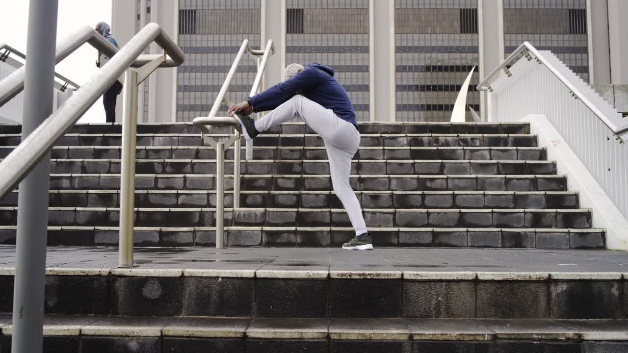Mature African American man stretching leg on handrail at stairs mirroring runner ascent