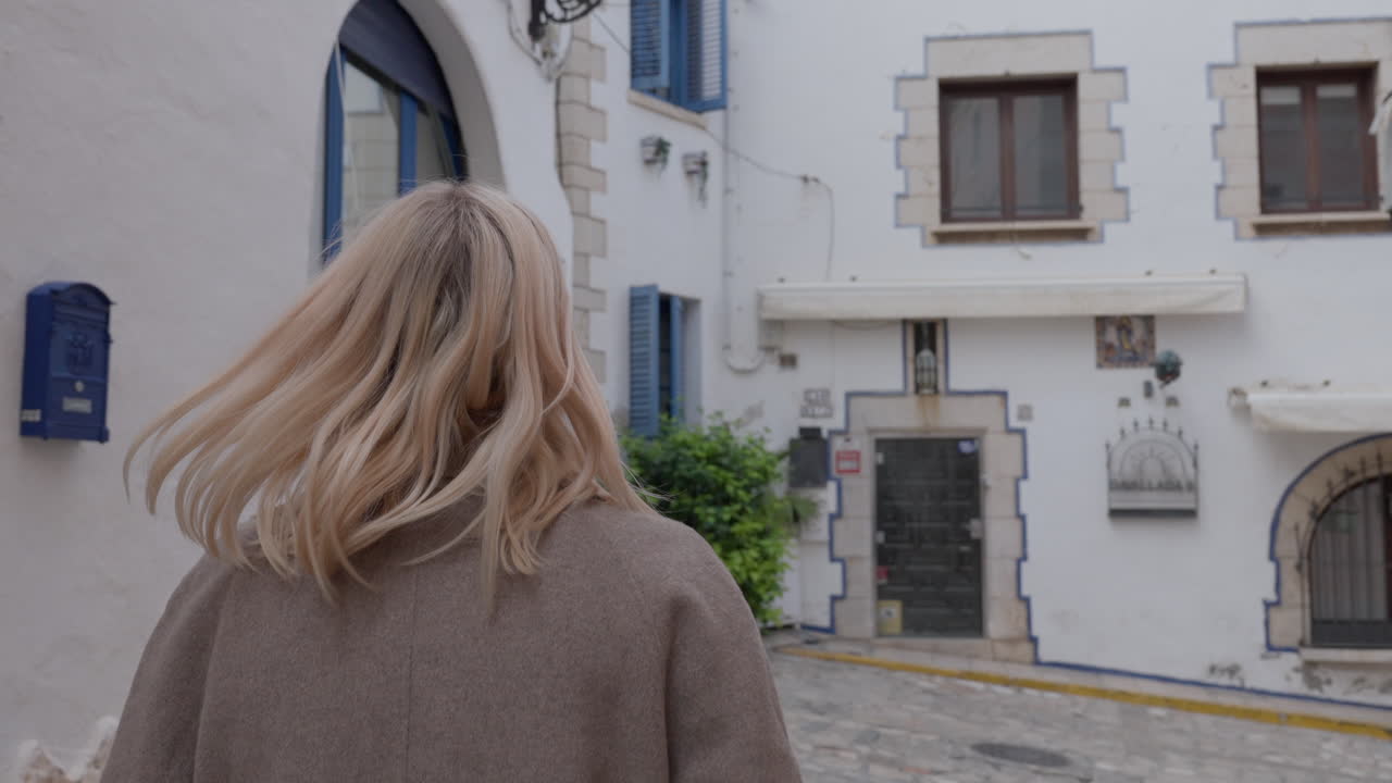 Blonde tourist woman is walking through old town streets wondering around admiring buildings.