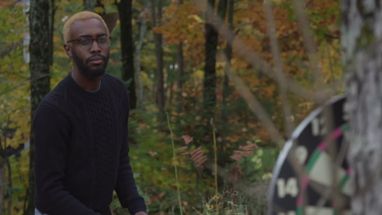 un hombre negro lanza un dardo a un tablero oscuro y luego sonríe