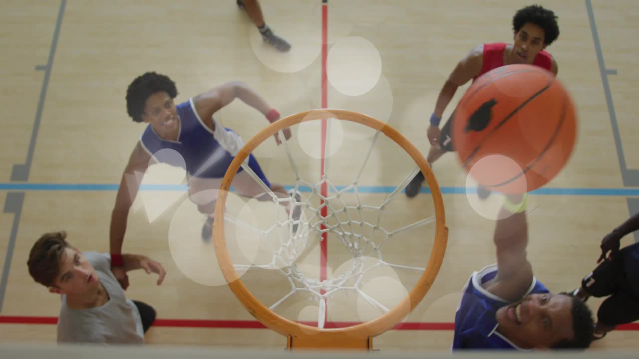 Un giocatore con la maglia rossa si dirige verso il canestro per segnare, attirando la difesa, mentre un altro giocatore con la maglia blu schiaccia la palla da basket nel canestro.