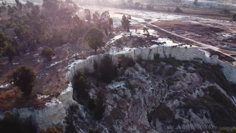 aerial drone shot tracking backwards over an old eroded mine dump as the golden rays from the morning sunrise casts a shadow on what remains of the history of the lucrative gold rush, south africa