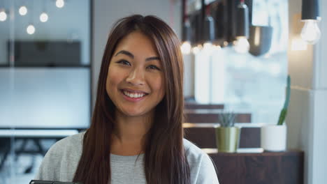 head and shoulders portrait of smiling asian businesswoman holding digital tablet in modern office