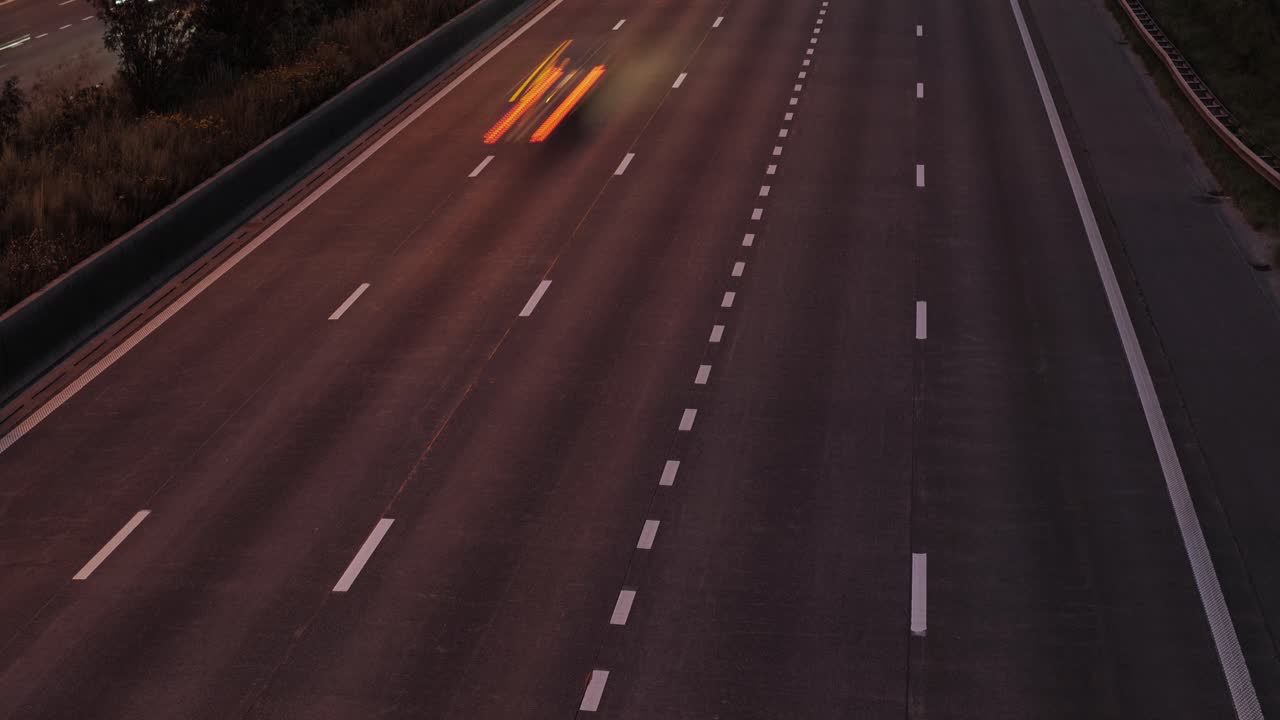 A timelapse view of nighttime highway traffic featuring red tail light motion trails and dynamic speed