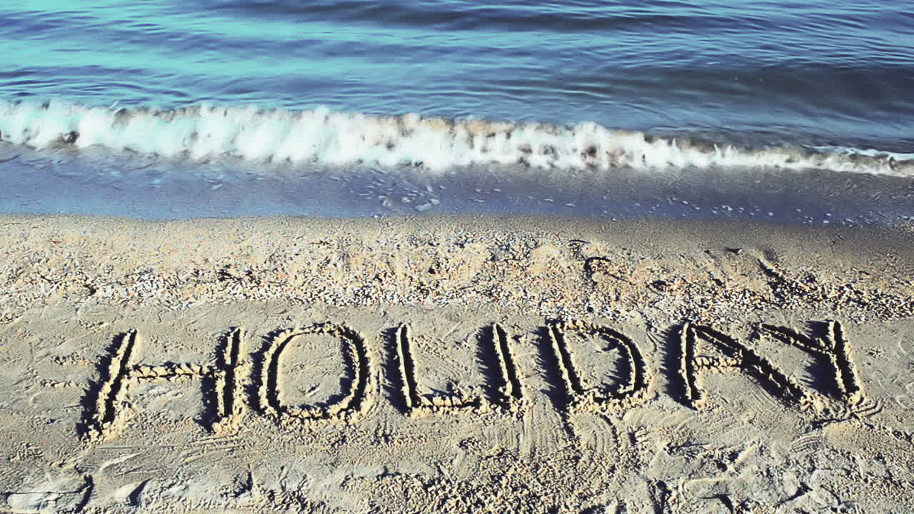Indskriften "Holiday" i sandet på stranden. Optagelse på stranden