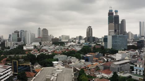 ascending drone shot showing downtown of jakarta city with high-rise buildings during grey cloudy day