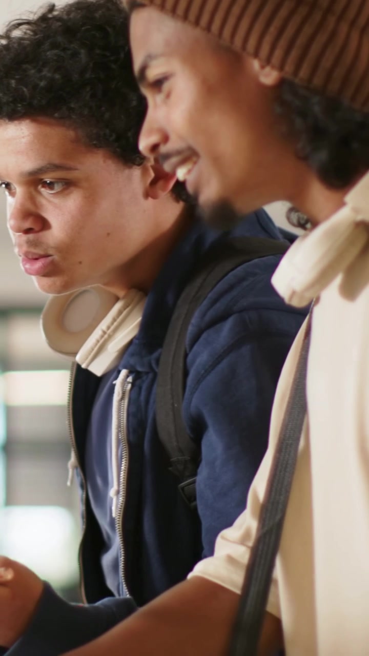 Vertical video: Leaning two adult men checking campus counter after offscreen hand pointing, beanie