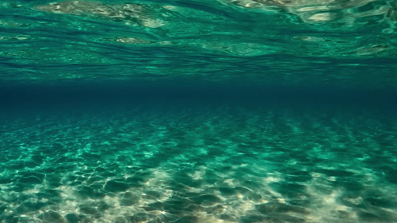 Authentic under water scene of crystalline turquoise tropical ocean water with rippled surface and reflections on seafloor with blue background