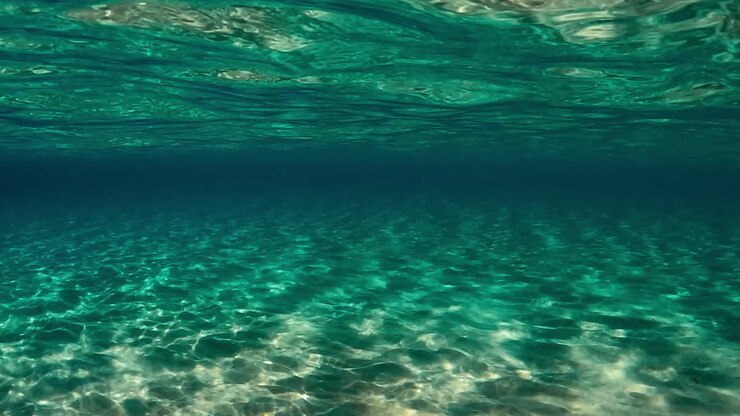 Authentic under water scene of crystalline turquoise tropical ocean water with rippled surface and reflections on seafloor with blue background