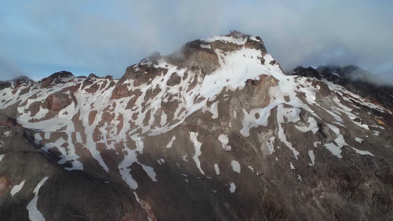 A breathtaking aerial dolly-in shot of Carihuairazo Volcano in Ecuador, partially covered in snow. The rugged volcanic landscape is revealed as the drone moves closer, capturing its majestic peaks.