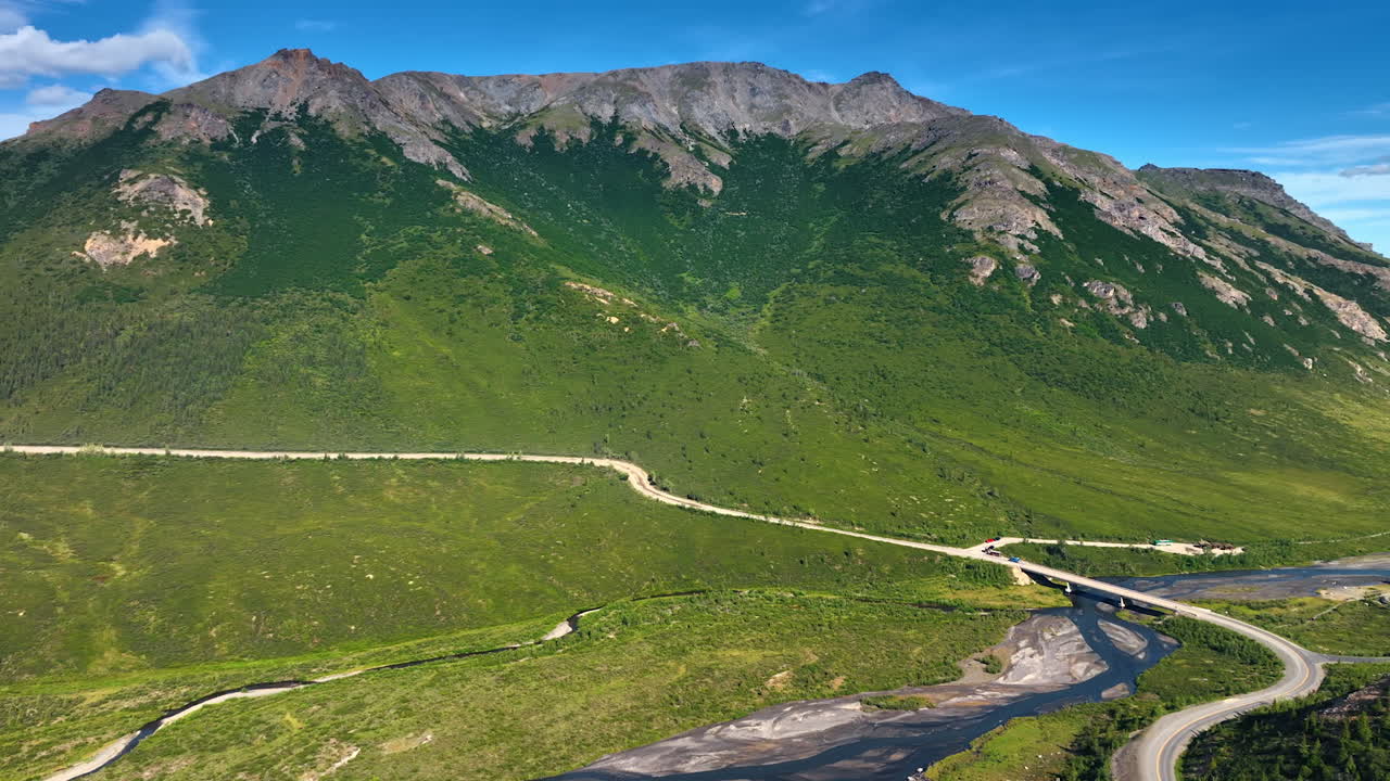 Mountainous landscape crossed by the river and highway with bridge. Drone footage over the natural scenery of Alaska, USA on sunny day