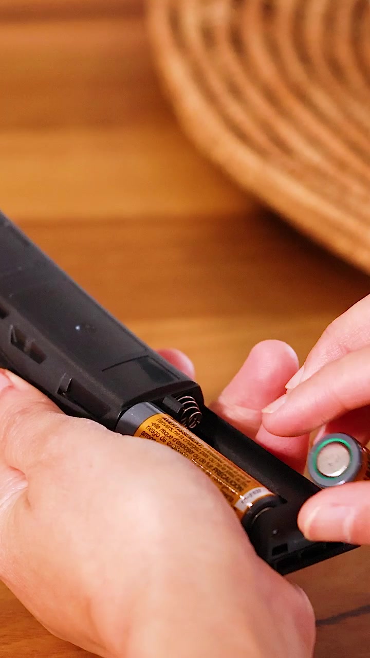 Mani sostituiscono le batterie in un telecomando su un tavolo di legno con illuminazione calda