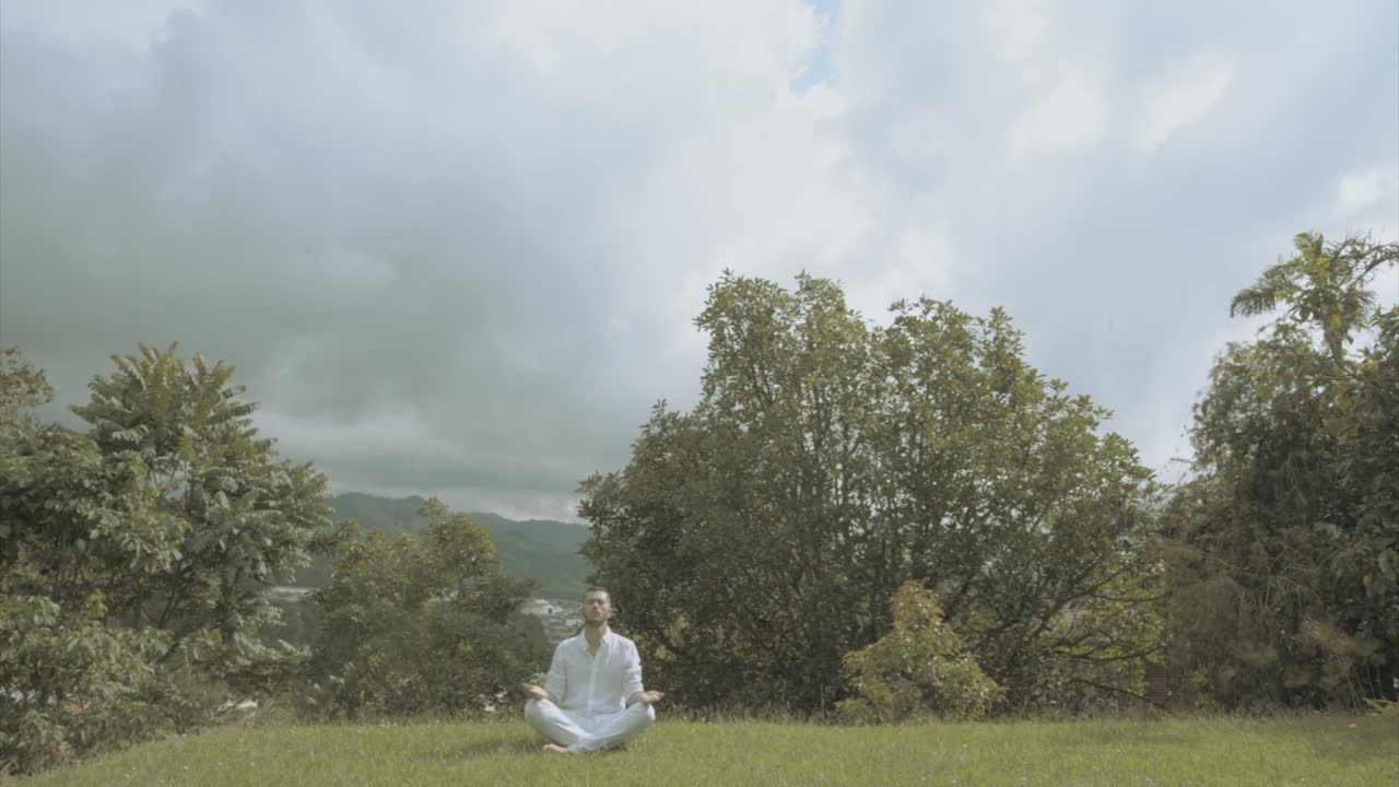Young man in white Dress doing yoga meditation and spiritual movements in a beautiful green landscape mindfulness and tai chi
