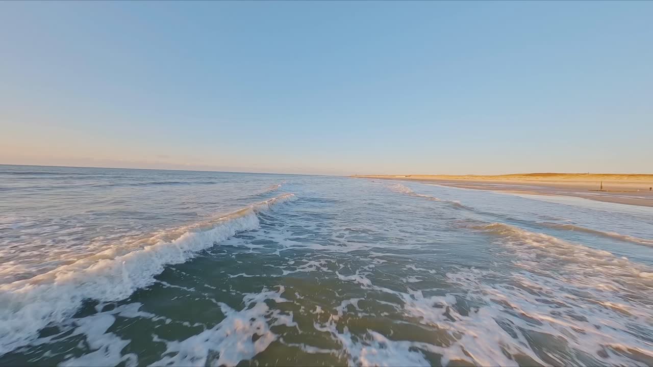 espectacular disparo de drones fpv volando de cerca sobre olas rompientes a alta velocidad durante la puesta de sol en un día sin nubes