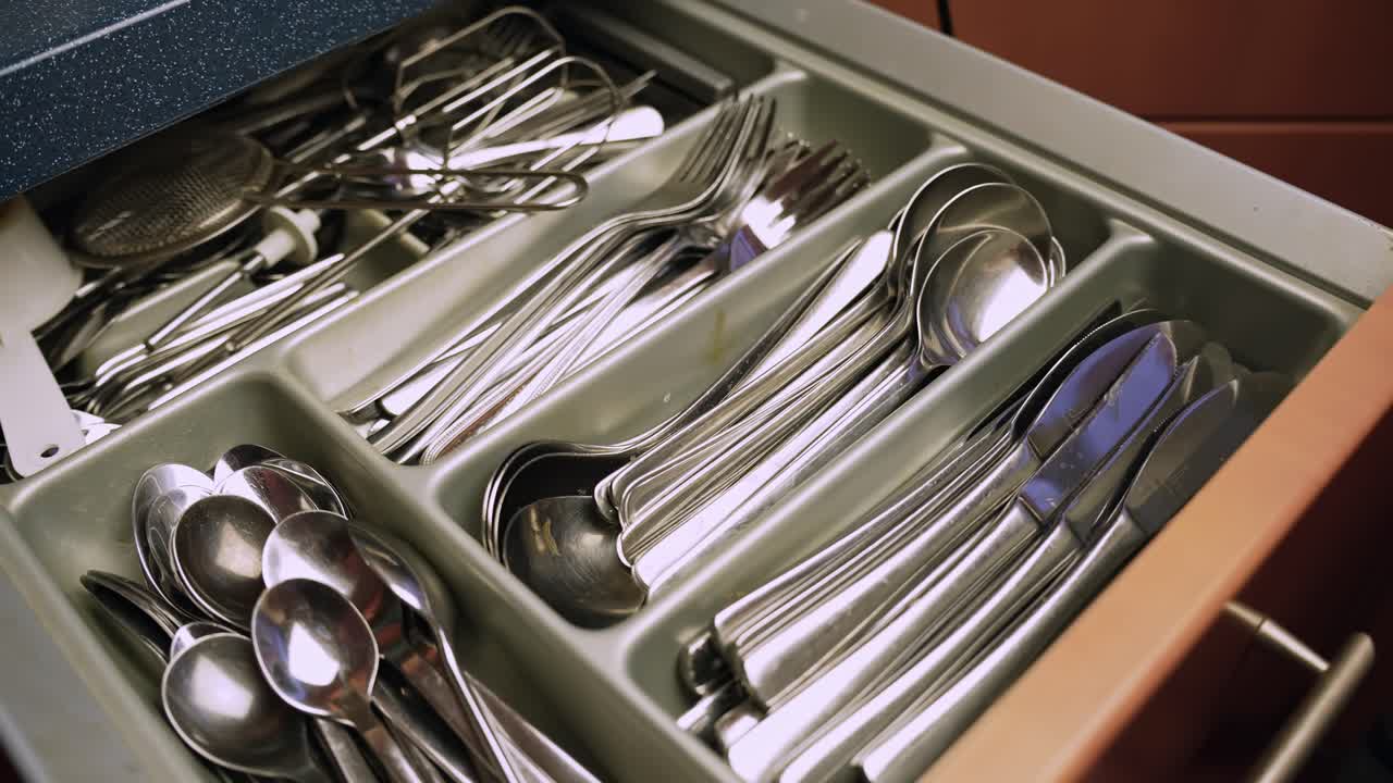Open kitchen drawer with neatly sorted stainless steel cutlery in a plastic organizer, spoons, forks and knives arranged for household storage and daily cooking routine