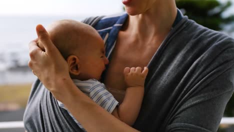 madre joven consolando a un bebé llorando en un sling en casa 4k