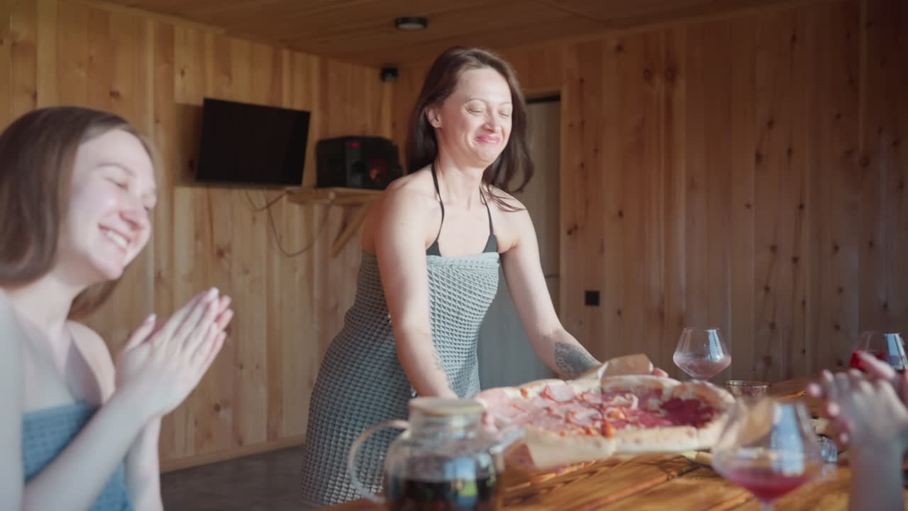 Happy woman showing her siblings pizza, holding pizza tray in hand, smiling as she drops it onto the table, cozy indoor setting with warm wooden walls, family moment full of joy and laughter